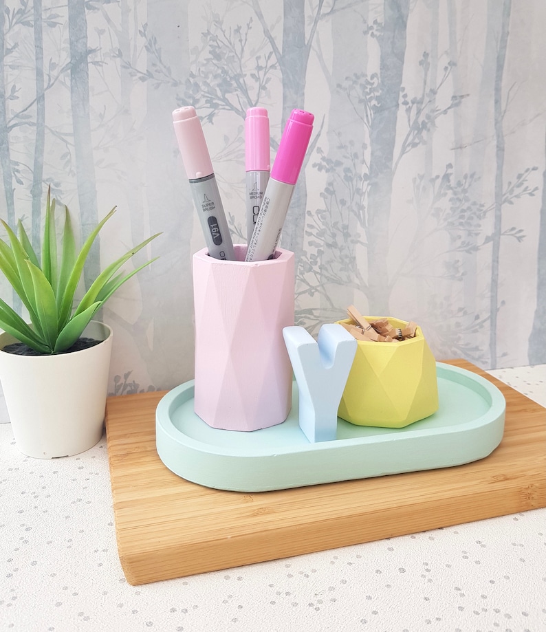 K&ouml;nnte beinhalten: Ein ovaler Schreibtisch-Organizer in Pastellgr&uuml;n mit einem geometrischen Stifthalter in Rosa, einem geometrischen Beh&auml;lter in Gelb und einem wei&szlig;en Buchstaben "Y".