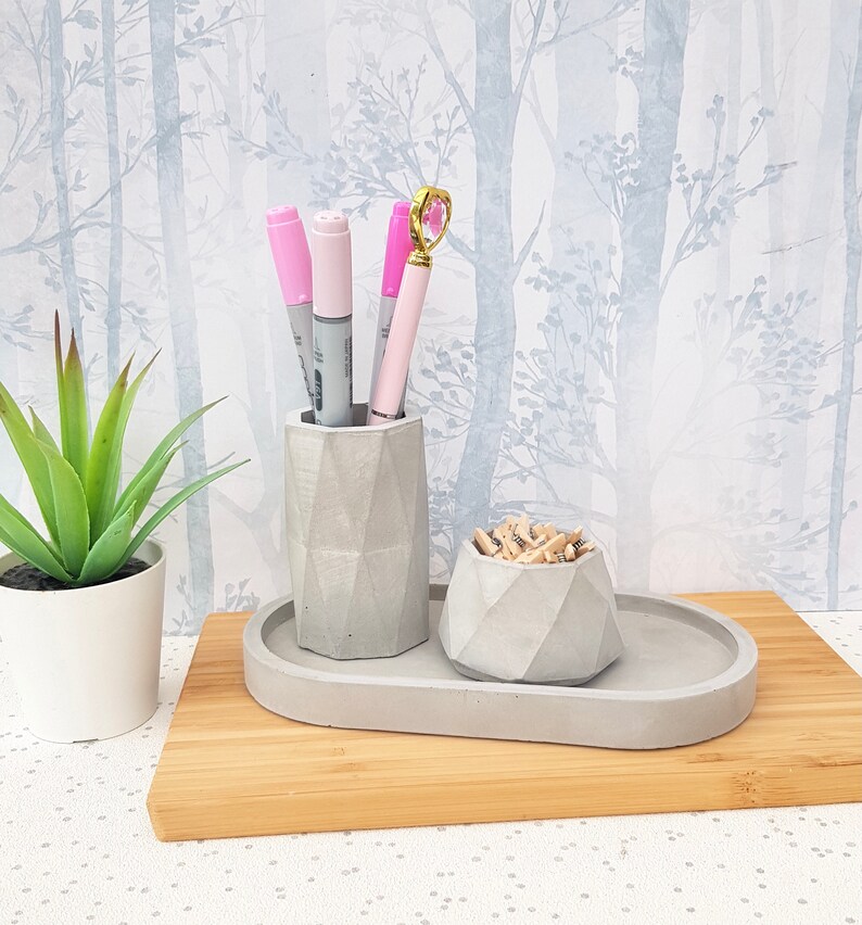 May include: A grey concrete desk organiser with a pen holder and a small bowl for paper clips. The organiser is on a wooden surface.