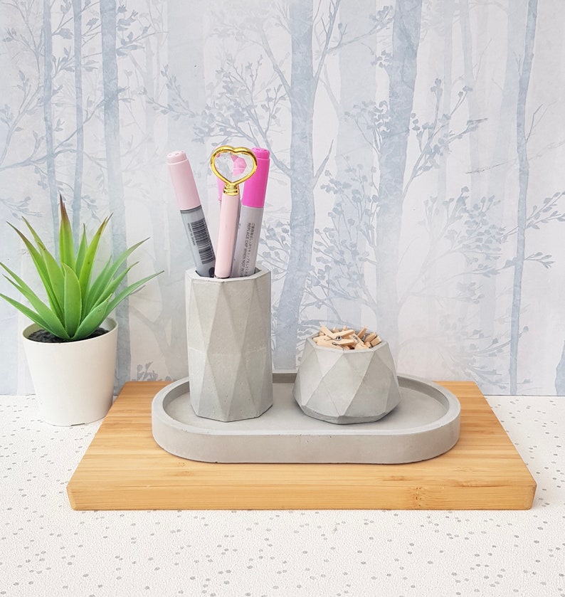 May include: A grey concrete desk organiser set with a pen holder, a small bowl for paper clips, and a tray. The set is on a wooden surface.