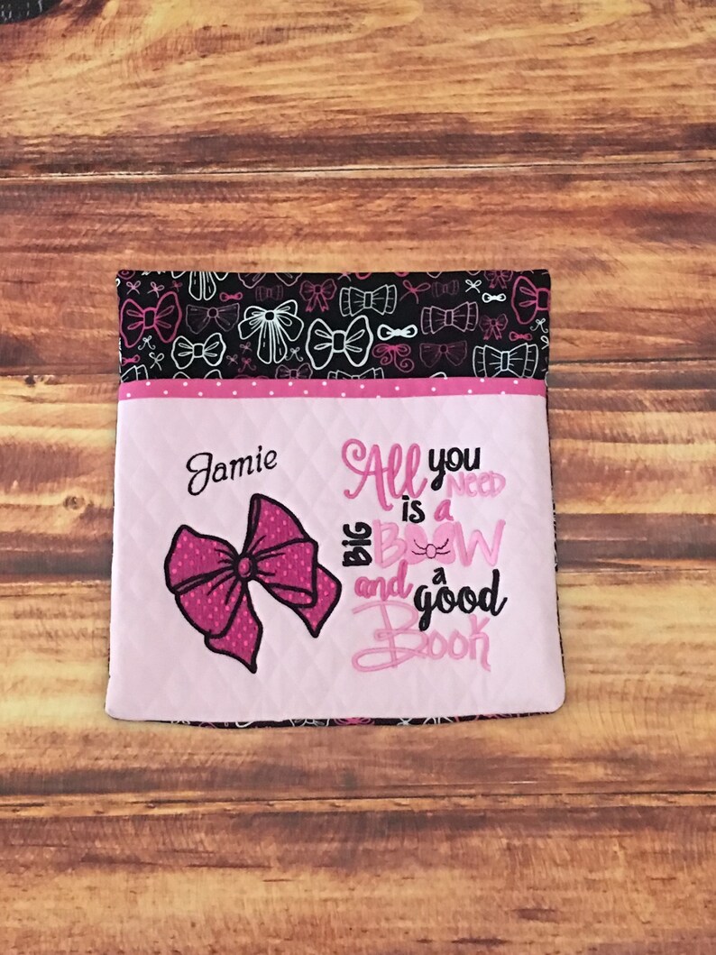 May include: Pink and black book bag with a pink bow and the text "All you need is a big bow and a good book" embroidered on the front. The bag is personalized with the name "Jamie".