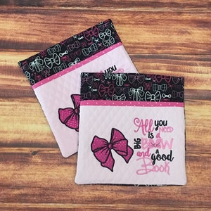 May include: Two pink and black quilted fabric pouches with a pink bow and the text "All you need is a big bow and a good book" on one pouch. The pouches are decorated with a black and white pattern of bows.