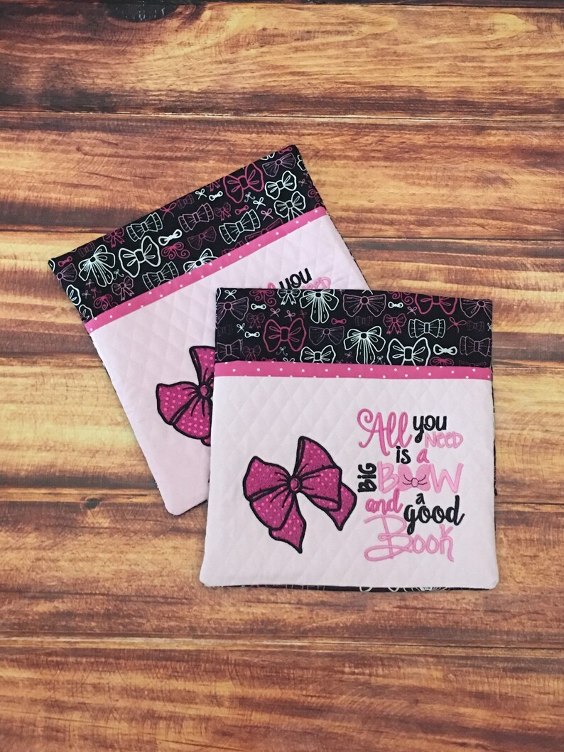 May include: Two pink and black quilted fabric pouches with a pink bow and the text "All you need is a big bow and a good book" on one pouch. The pouches are decorated with a black and white pattern of bows.