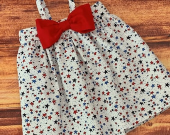 May include: A white sleeveless dress with a red bow and a blue and red star pattern.
