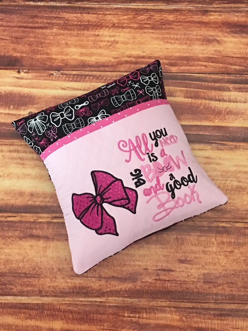 May include: Pink and black pillow with a pink bow and the text "All you need is a big bow and a good book".