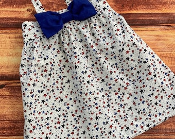 May include: A white sleeveless dress with a blue bow at the neckline. The dress is covered in a pattern of red, blue, and black stars.