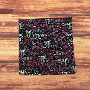 May include: Black fabric with a white and pink bow pattern. The bows are of various sizes and are arranged in a random pattern.