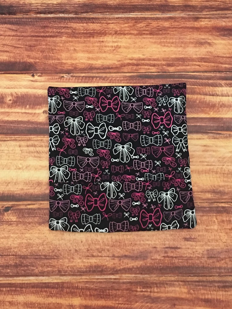 May include: Black fabric with a white and pink bow pattern. The bows are of various sizes and are arranged in a random pattern.