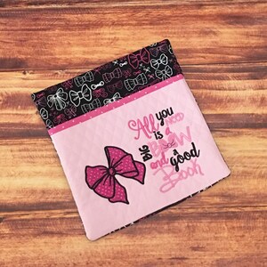 May include: Pink fabric pouch with a large pink bow and the text "All you need is a big bow and a good book". The pouch is lined with black fabric with a white bow pattern.