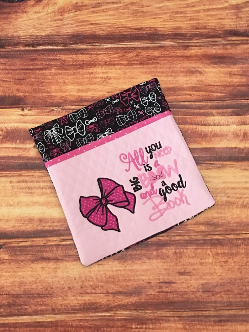 May include: Pink fabric pouch with a large pink bow and the text "All you need is a big bow and a good book". The pouch is lined with black fabric with a white bow pattern.