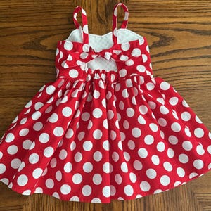 May include: A red and white polka dot dress with spaghetti straps and a bow detail on the back. The dress has a gathered skirt and a white checkered pattern on the inside of the bodice.