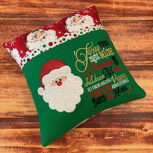 K&ouml;nnte beinhalten: Ein weihnachtliches Kissen mit gr&uuml;nem Grund und einem rot-wei&szlig; gemusterten Oberteil. Das Kissen zeigt einen gestickten Weihnachtsmann und den Text "Twas the night before Christmas..." in Gold-, Rot- und Gr&uuml;nt&ouml;nen.