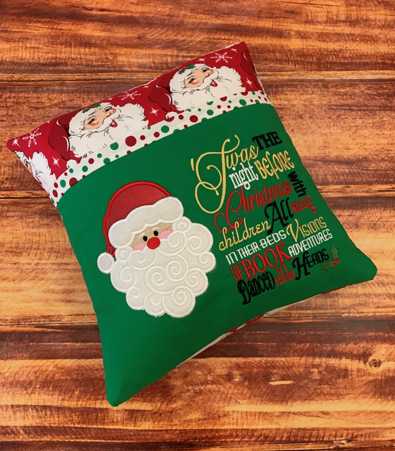 K&ouml;nnte beinhalten: Ein weihnachtliches Kissen mit gr&uuml;nem Grund und einem rot-wei&szlig; gemusterten Oberteil. Das Kissen zeigt einen gestickten Weihnachtsmann und den Text "Twas the night before Christmas..." in Gold-, Rot- und Gr&uuml;nt&ouml;nen.