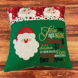 K&ouml;nnte beinhalten: Ein weihnachtliches Kissen mit gr&uuml;nem Grund und einem rot-wei&szlig; gemusterten Oberteil. Es zeigt einen gestickten Weihnachtsmann und den Text "Twas the night before Christmas".