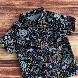 Puede incluir: Una camisa negra de botones con un estampado de temática científica. El estampado presenta ilustraciones coloridas de fórmulas químicas, átomos y otros símbolos científicos.