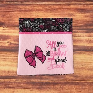 May include: Pink fabric pouch with a black and white bow pattern on the back. The front of the pouch is pink with a large pink bow and the text "All you need is a big bow and a good book".