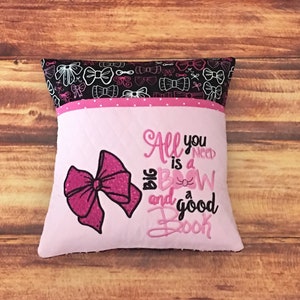 May include: Pink and black pillow with a pink bow and the text "All you need is a big bow and a good book".