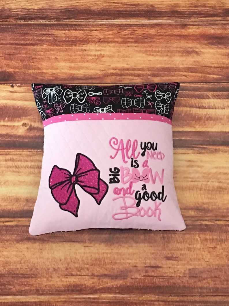 May include: Pink and black pillow with a pink bow and the text "All you need is a big bow and a good book".