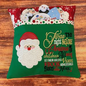 K&ouml;nnte beinhalten: Ein gr&uuml;nes Weihnachtskissen mit einem Santa Claus-Applikation und dem gestickten Text "Twas the night before Christmas". Das Kissen hat eine Tasche, die mit weihnachtlichen Gegenst&auml;nden gef&uuml;llt ist. Der obere Rand ist rot mit wei&szlig;en Punkten und Santa Claus-Illustrationen.