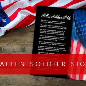 Może przedstawiać: Czarno-biały znak z tekstem "Fallen Soldier Table" i opisem symboliki stołu. Znak znajduje się na drewnianej powierzchni, na której leży rozłożona amerykańska flaga.