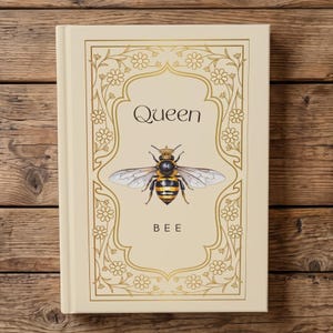 Könnte beinhalten: Ein cremefarbenes Hardcover-Buch mit einer zentralen Illustration einer Biene, die eine kleine Krone trägt. Der Text "Queen" steht über der Biene und "BEE" darunter. Der Einband ist mit einem goldfarbenen floralen Randdesign verziert.