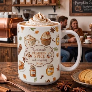 May include: A white ceramic mug filled with coffee topped with whipped cream, featuring a pattern of autumn leaves, a cupcake, a jar of honey, and a pumpkin spice jar. The center text reads: God made PUMPKIN SPICE and everything Nice.