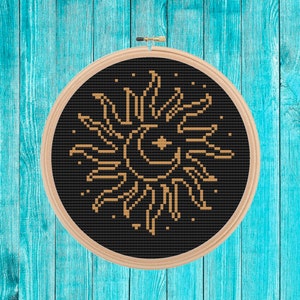May include: A black and gold embroidery hoop with a sun and moon design. The sun has a crescent moon shape inside of it.
