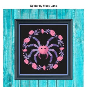 May include: A cross-stitch pattern of a pink spider with purple legs surrounded by a wreath of pink flowers and leaves on a black background. The title "Spider by Moxy Lane" is at the top of the image.