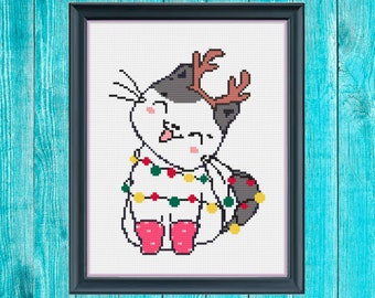 May include: A white cat with black ears and a gray patch on its back is wearing a red and green Christmas lights garland and a brown reindeer antler headband. The cat is sitting with its tongue sticking out and wearing red and white socks.