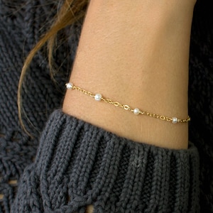 May include: A delicate gold chain bracelet with small white pearls. The bracelet is on a person's wrist.