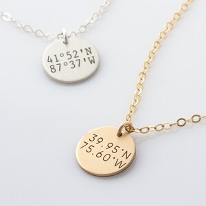 Puede incluir: Dos collares con colgantes redondos. El colgante de la cadena plateada tiene las coordenadas "41°52'N 87°37'W" grabadas en él. El colgante de la cadena dorada tiene las coordenadas "39.95'N 75.60'W" grabadas en él.