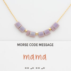 May include: A gold chain necklace with a message in morse code spelled out in purple beads. The message is "mama" and the morse code is "-- .- -- .--".