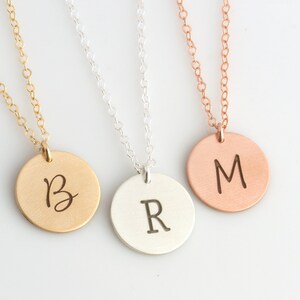May include: Three necklaces in gold, silver, and rose gold with round pendants featuring the letters B, R, and M.
