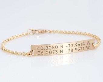 May include: Gold chain bracelet with a rectangular tag engraved with the coordinates "40.8050 N -73.9614 W 36.0073 N -78.9371 W".