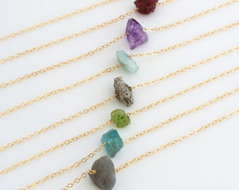 May include: A set of nine gold chains with different colored gemstones attached. The gemstones are in various shapes and sizes, including a pink stone, a red stone, a purple stone, a light blue stone, a dark gray stone, a gold stone, a green stone, a blue stone, and a gray stone.