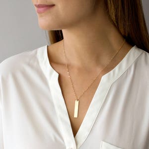 May include: A gold chain necklace with a long, thin, rectangular pendant.