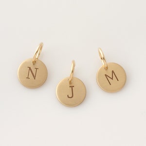 May include: Three gold-colored metal charms with initial letters N, J, and M engraved on them.