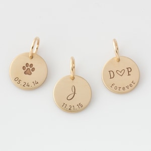 May include: Three gold-toned round charms with engraved text and designs. The first charm has a paw print and the text "05.24.14". The second charm has the letter "J" and the text "11.21.15". The third charm has the text "D♥P forever".