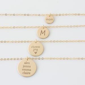 May include: Four gold necklaces with different charms. The top necklace has a charm that says "mom". The second necklace has a charm with the letter "M". The third necklace has a charm that says "choose joy" with a small heart symbol. The bottom necklace has a charm that says "alex jenna emma claire".
