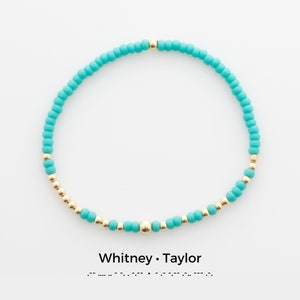 May include: A turquoise and gold beaded bracelet with the text "Whitney · Taylor" below.