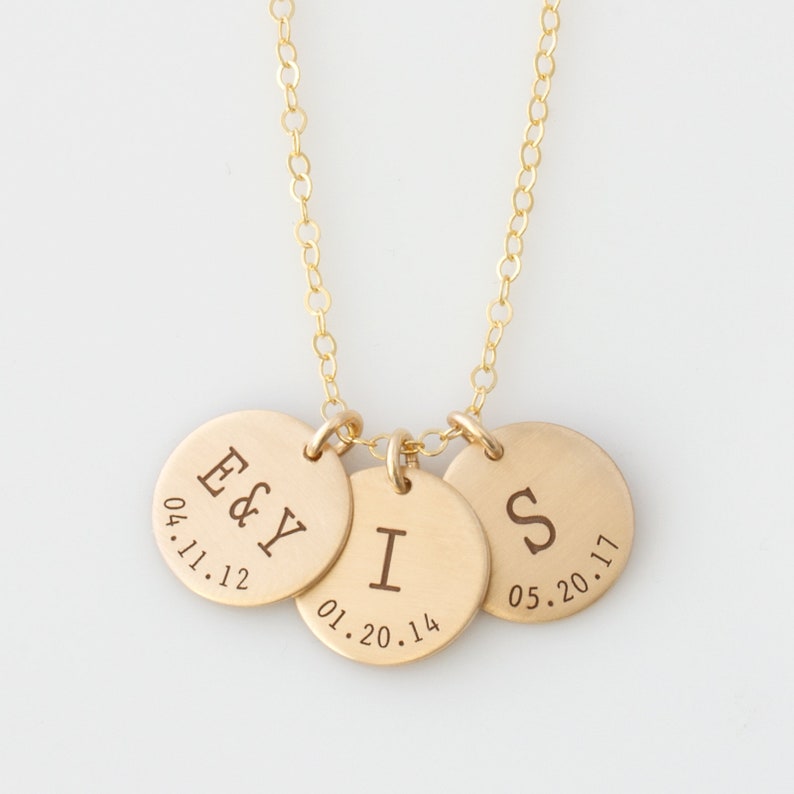 May include: Gold necklace with three round charms. The charms are engraved with the letters "E & Y", "I", and "S" and dates "04.11.12", "01.20.14", and "05.20.17".