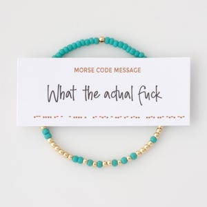 Peut inclure: Un bracelet de perles turquoise et dorées avec une carte blanche sur laquelle on peut lire "MORSE CODE MESSAGE" et "What the actual fuck". Le bracelet est composé de petites perles turquoise et de perles dorées. La carte contient également une ligne de code Morse.