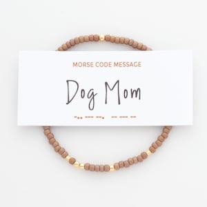 May include: A brown beaded bracelet with gold beads and a card that reads "Morse Code Message Dog Mom" with the Morse code for "Dog Mom" underneath.