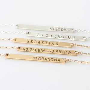 Puede incluir: Cuatro collares de barra de oro y plata con diferentes textos grabados. El collar superior dice "SISTERS". El segundo collar dice "S+C=L♡C♡J". El tercer collar dice "SEBASTIAN". El cuarto collar dice "40.7308&deg;N -73.9871&deg;W" y "♡GRANDMA".