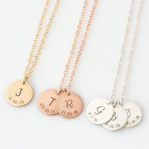 May include: Three gold necklaces with personalized round pendants. The pendants are engraved with initials and dates. The necklaces are in gold, rose gold, and silver.