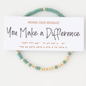 May include: A teal and gold beaded bracelet with a card that reads "You Make a Difference" in cursive. The card also has the message in Morse code. The bracelet is made of small, round beads.
