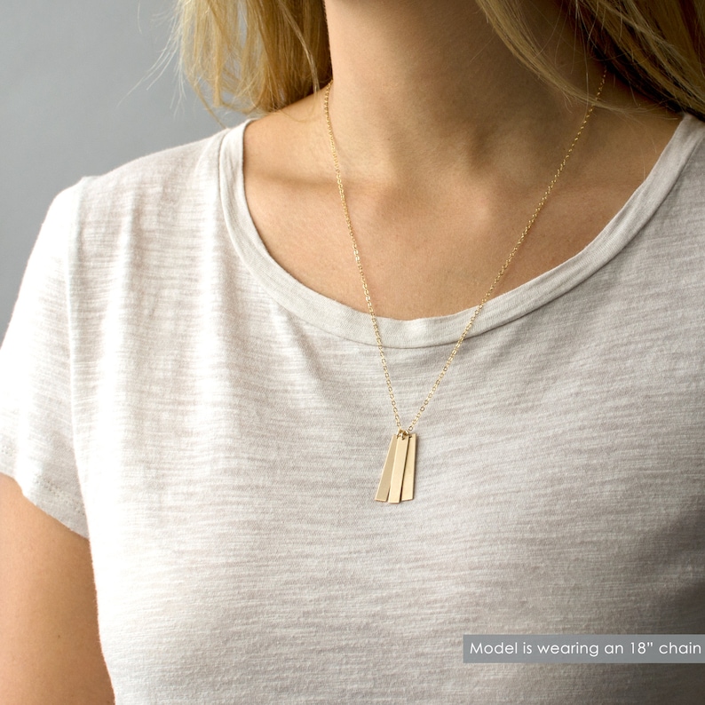 May include: A gold chain necklace with three thin, rectangular gold pendants. The model is wearing an 18" chain.