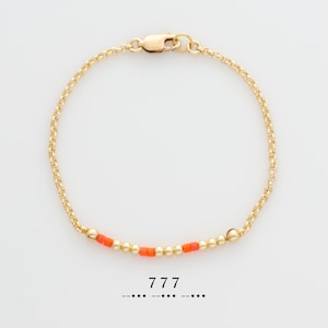May include: A gold chain bracelet with a row of small orange beads. The bracelet has a clasp closure. The text "777" is printed below the bracelet.