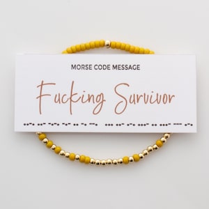 May include: A yellow beaded bracelet with gold beads. The bracelet has a card attached to it that says "Morse Code Message" and "Fucking Survivor" in brown text. The card also has a line of dots and dashes representing the message in Morse code.