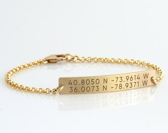 May include: A gold chain bracelet with a rectangular tag engraved with the coordinates "40.8050 N-73.9614 W 36.0073 N-78.9371 W".