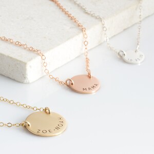 May include: Three gold necklaces with round pendants. The pendants are engraved with the words "MAMA", "ZOE.NOAH", and "10.23.10".